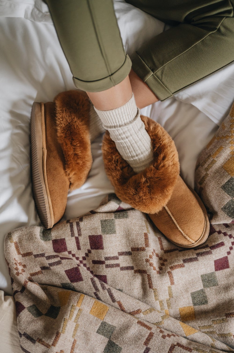 orange/brown sheepskin slipper boots with a fluffy cuff, being worn on a bed