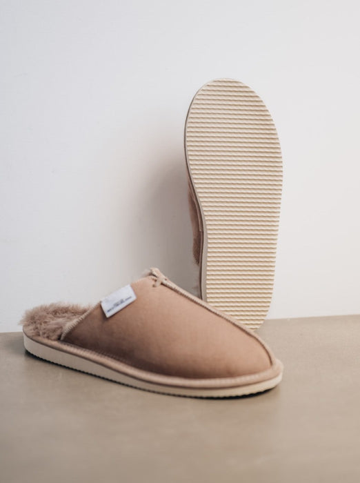 stone coloured sheepskin slippers placed against wall to show off EVA foam sole from below