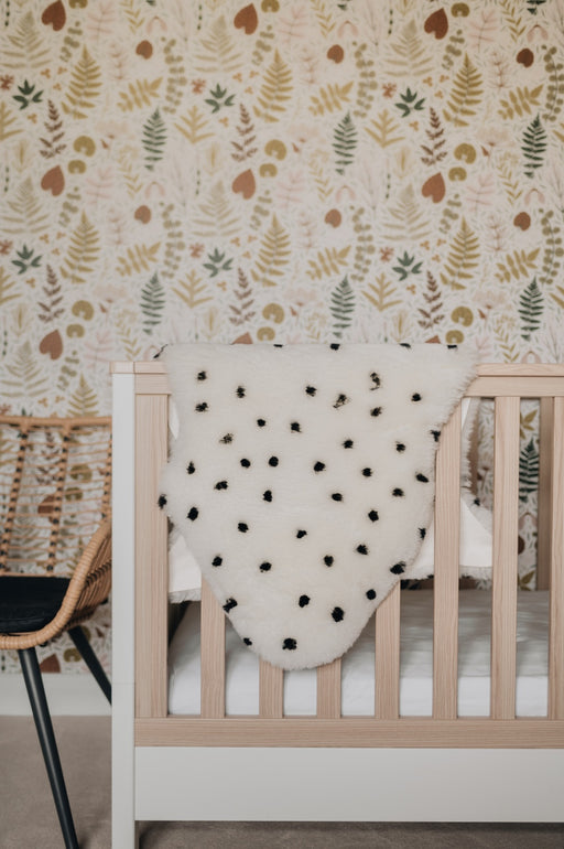 Sheepskin Nursing rug in Ivory Polka Dot draped over a cot in a nursery