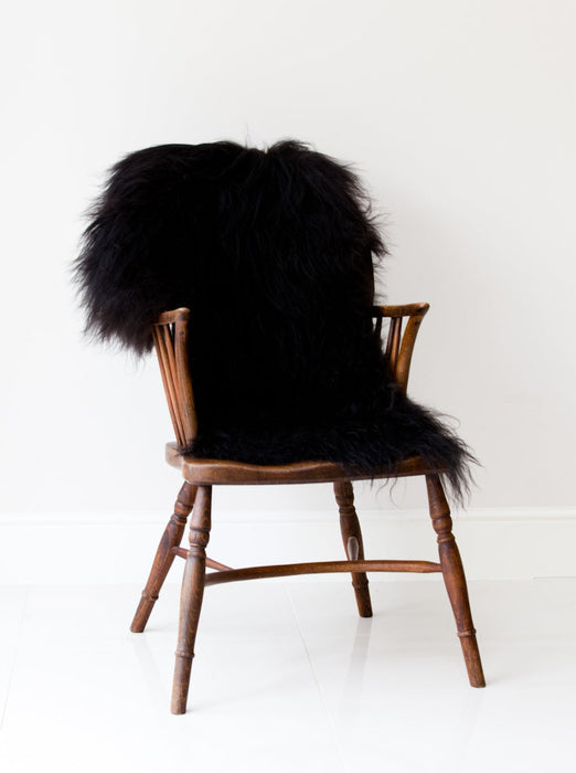 A deep black/brown Icelandic Sheepskin Long Wool Rug. Draped over a brown wooden chair.
