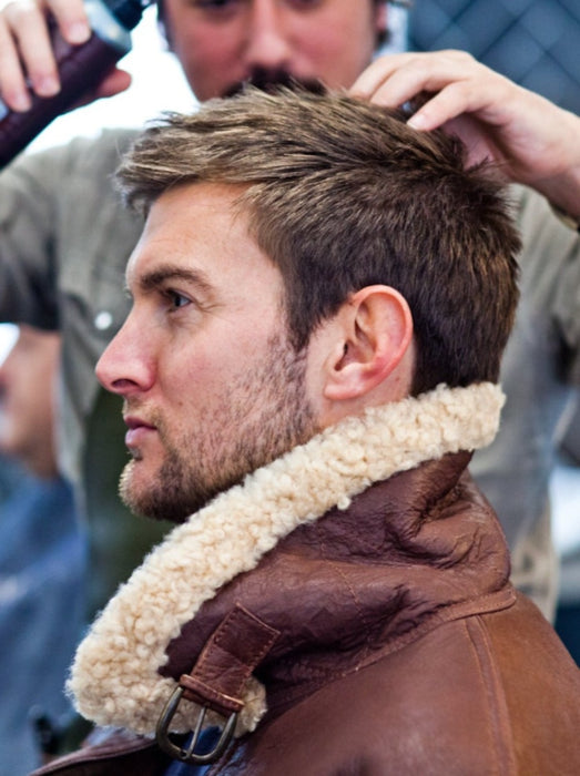Man sat in barbers chair having his hair done, wearing a Men's Brown Sheepskin Aviator Jacket with a turned up Sheepskin collar.