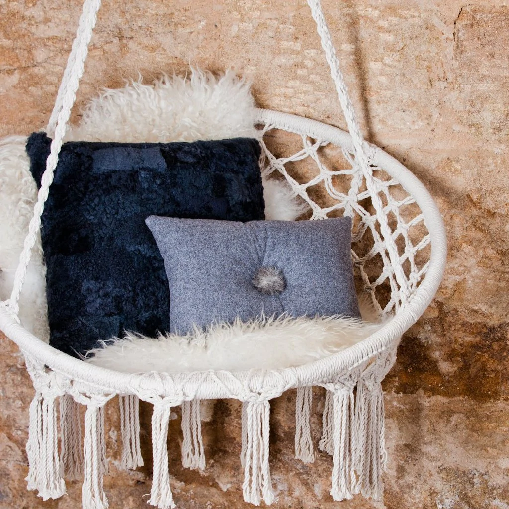 Anita Wool Cushion in grey, and Alice Sheepskin Cushion in Charcoal Grey. Featured on a swingseat. 