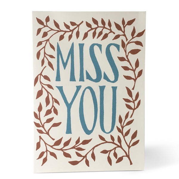 Miss You Greetings Card. A verticle card, features a simple brown leafy edge design. At the centre of the card in large blue text reads 'Miss You'. Comes with an envelope.