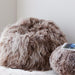 A taupe long wool Icelandic Sheepskin Bean bag features the image, with a smaller ottoman next to it.