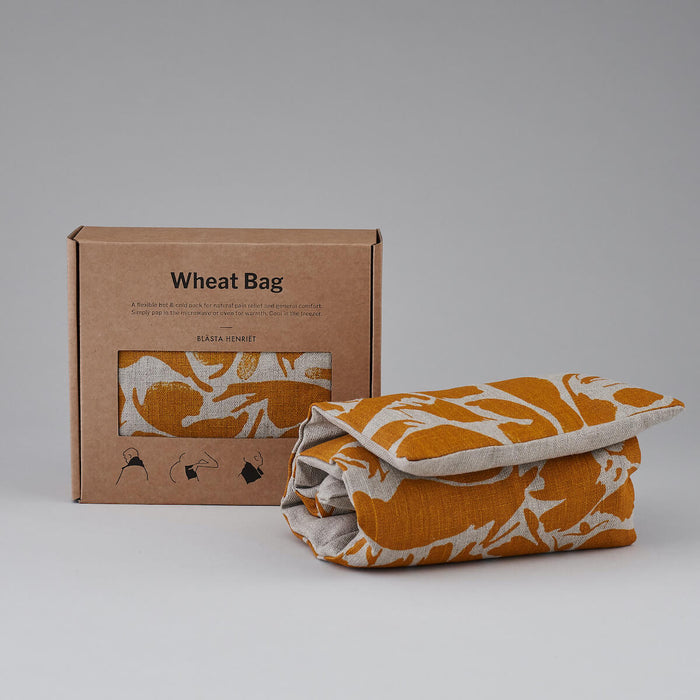 Folded Yellow Small Creatures Abstract Pattern Blästa Henriët Wheat Bag. Next to it, a boxed Wheat Bag in Brown Cardboard Packaging.