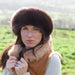 A female model holds the front of her Sheepskin jacket, she wears a brown Sheepskin hat. The hat is soft and thick and comes down over her ears.