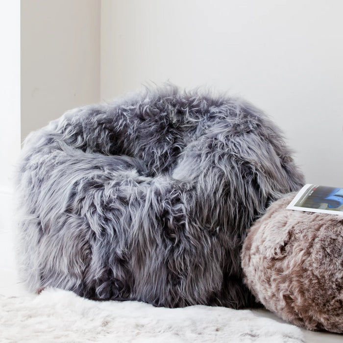 Wide shot image of a large grey long wool Icelandic Bean Bag. Featured next to it is a smaller taupe sheepskin footrest.