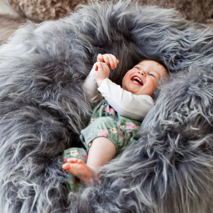 A laughing child lays on top of a grey long wool Icelandic Sheepskin Beanbag.
