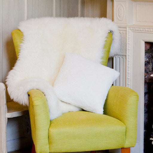 Alice Sheepskin Cushion, in White. Displayed on a yellow chair, with a white Sheepskin Rug draped over the top.