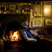 Male model wears Men's Sheepskin Gilet in pub, sat next to blazing fireplace.