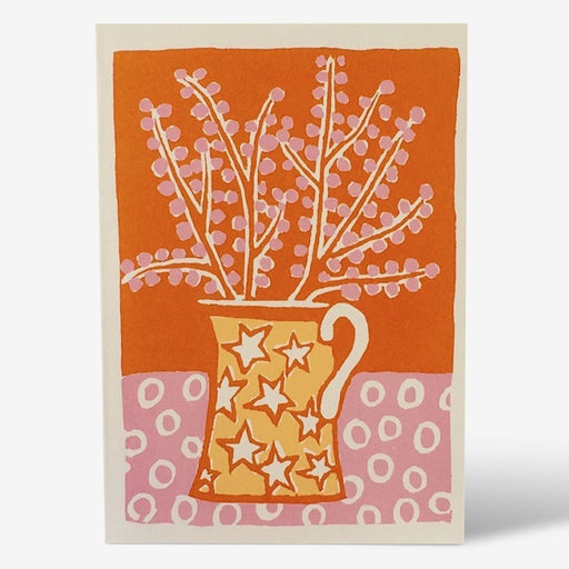 Jug & Blossom greetings card. A verticle card, featuring a print of pink bobbly flowers in a yellow star printed handled jar. The background is orange with a pink table with circle shapes. Comes with an envelope.