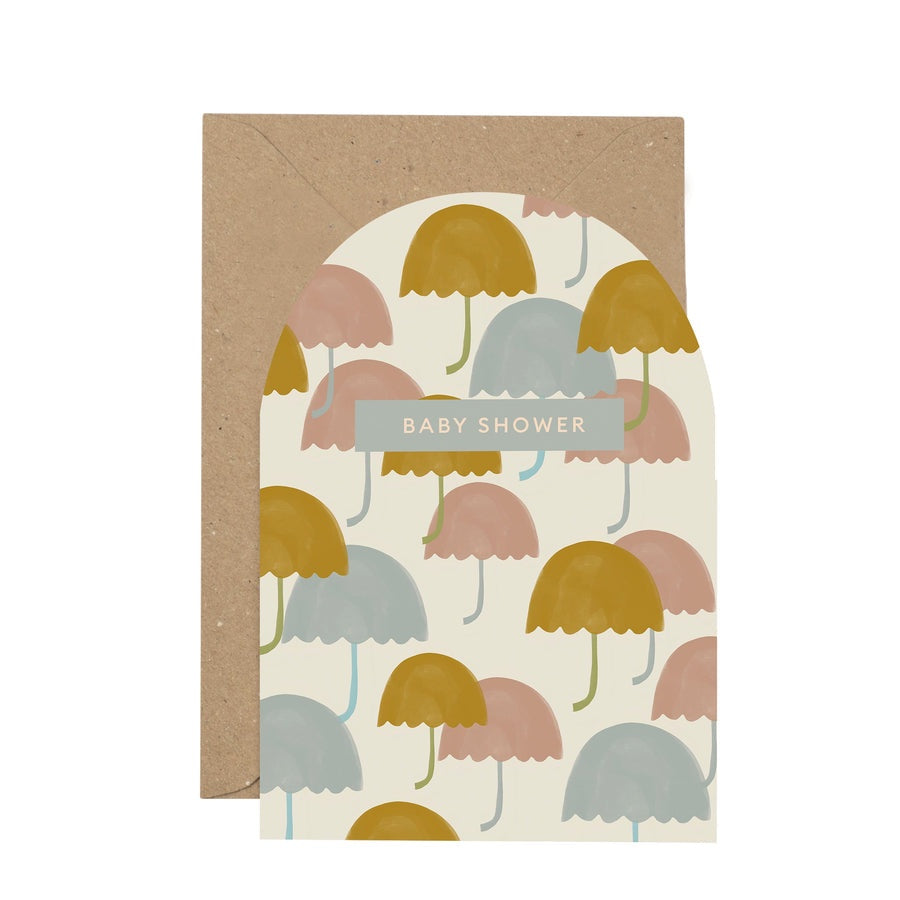 'Baby Shower' Curved Card. A white background with mustard yellow, baby blue and soft pink umbrellas dotted over the front of the card. Features a small blue rectandle with the writing 'Baby Shower'. Comes with an envelope.