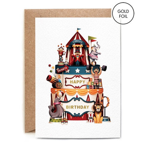 Circus Cake Birthday Card. A vertical rectangular card, with a white background. Features a fun gold foil Circus themed birthday cake, with animal decorations and a circus tent at the top. On the cake reads 'Happy Birthday' in green writing. Comes with an envelope.