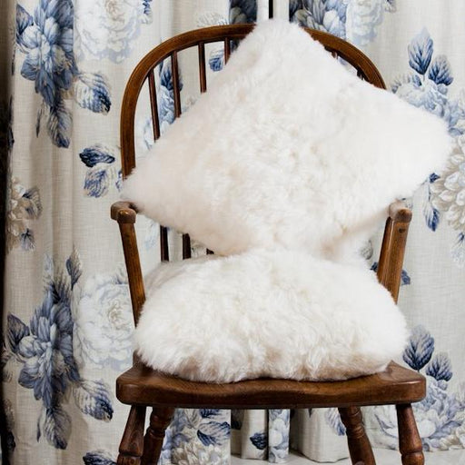 Icelandic Sheepskin Cushion in White, on wooden chair against floral background.