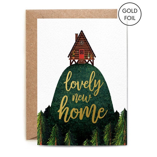 Lovely New Home Card. A verticle card, features a wooden hut on stilts on top of a large green hill with trees lining the bottom. On the hill in gold foil writing reads 'Lovely New Home'. Comes with an envelope.